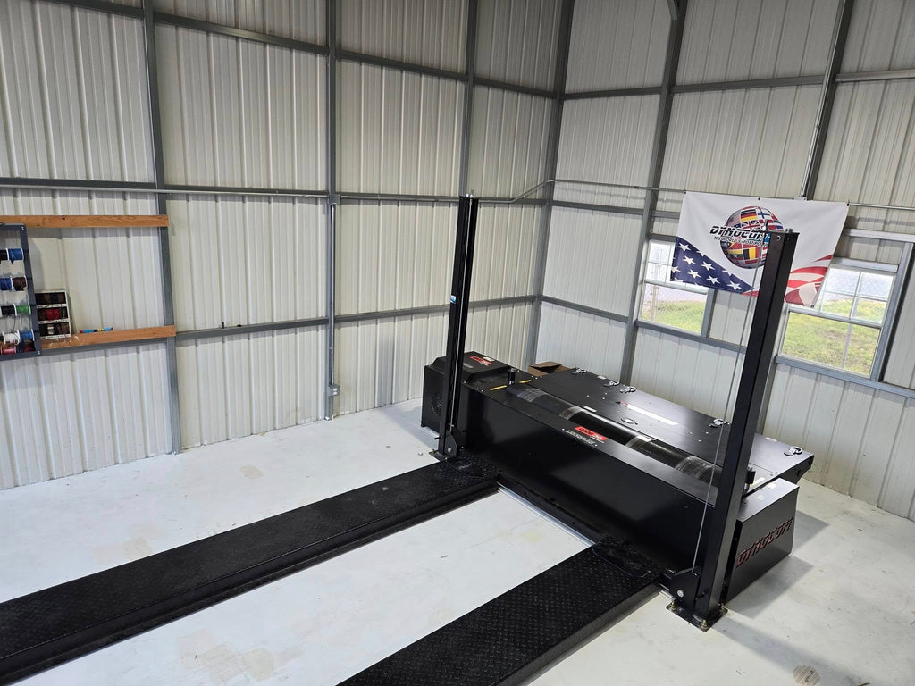 Dynocom 2WD 8000 Series chassis dynamometer installed in metal shop building with Dynocom Racing banner