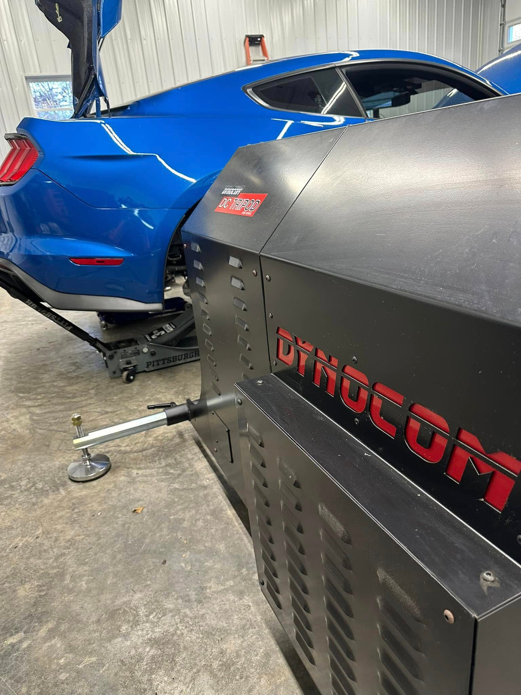 Dynocom DC TriPod close-up showing branding and hub connection on blue Mustang