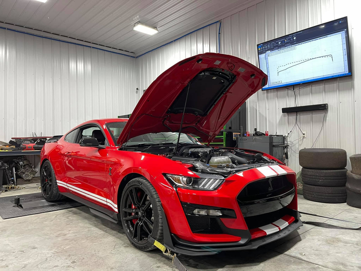 Red Shelby GT500 with hood open on Dynocom 21,000 Series dyno with power curve displayed on monitor