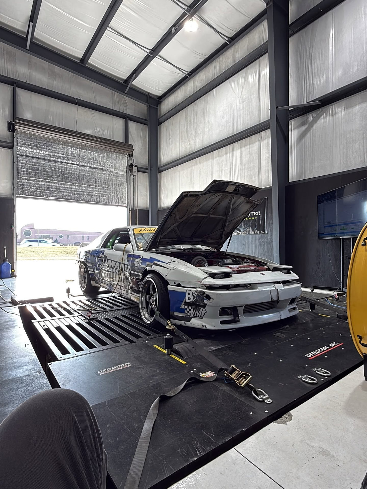 Nissan S13 drift car with hood open on Dynocom AWD 8000 series dynamometer in metal performance shop