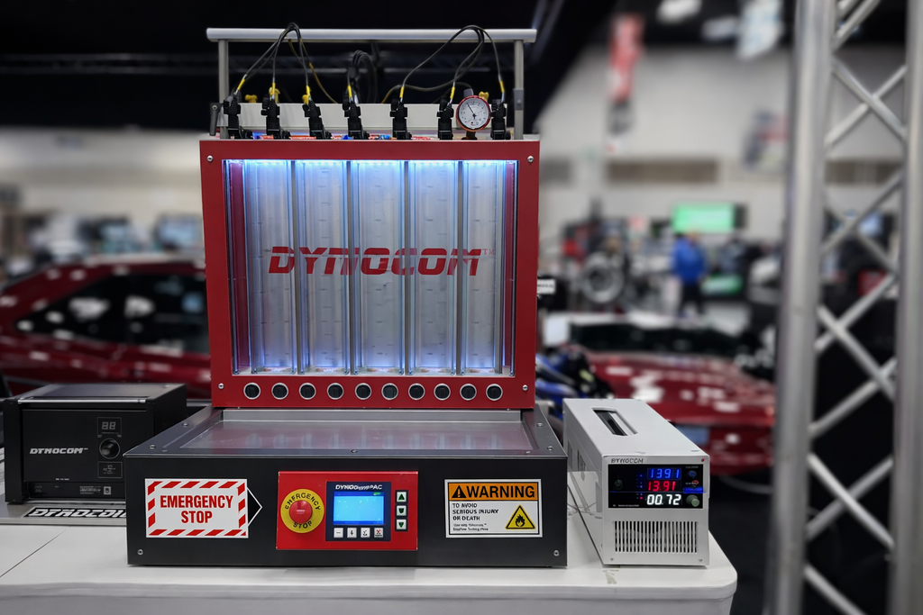 Dynocom AIC-8 injector test bench with red frame, backlit chambers, and DYNODynePAC controller on display at trade show