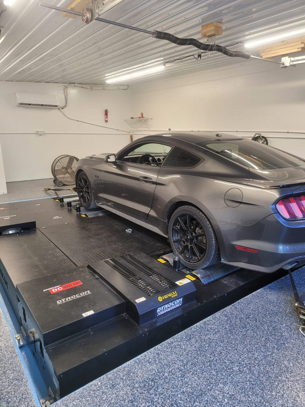 Grey Ford Mustang GT strapped on Dynocom DC 6000 AWD dynamometer in performance tuning shop